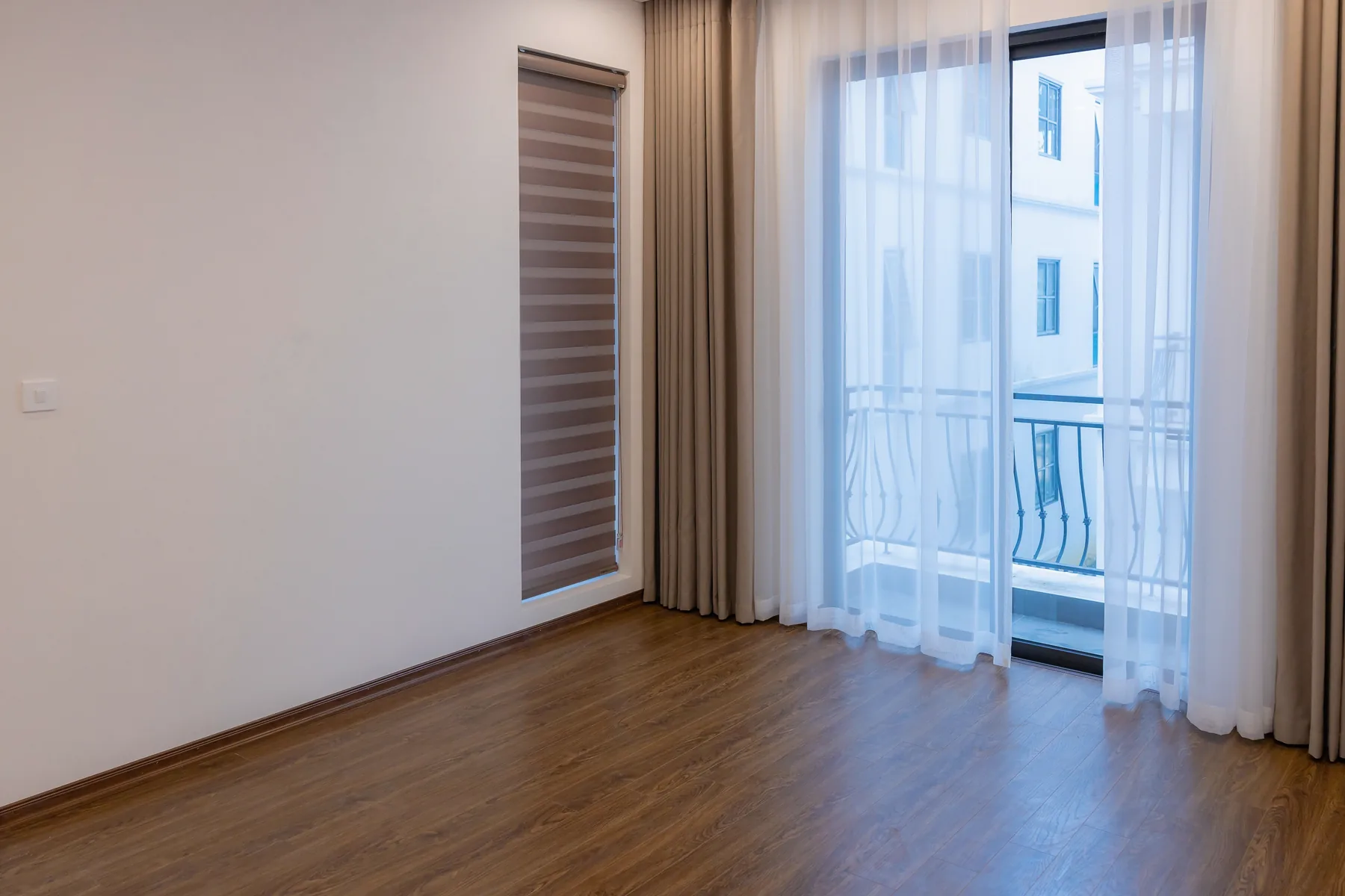 Heller leerer Wohnraum mit Holzfußboden und kleinem Balkon